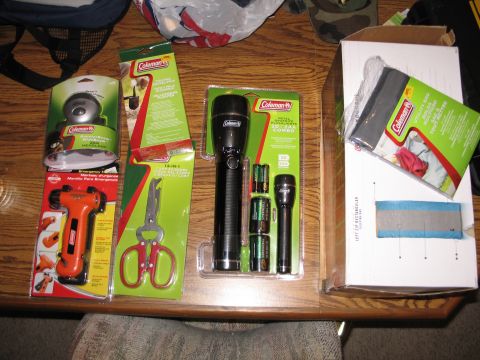 1995 Ford Bronco - Various Coleman brand items including flashlights, a headlamp, an emergency hammer, and multi-tool scissors are laid out on a wooden table.