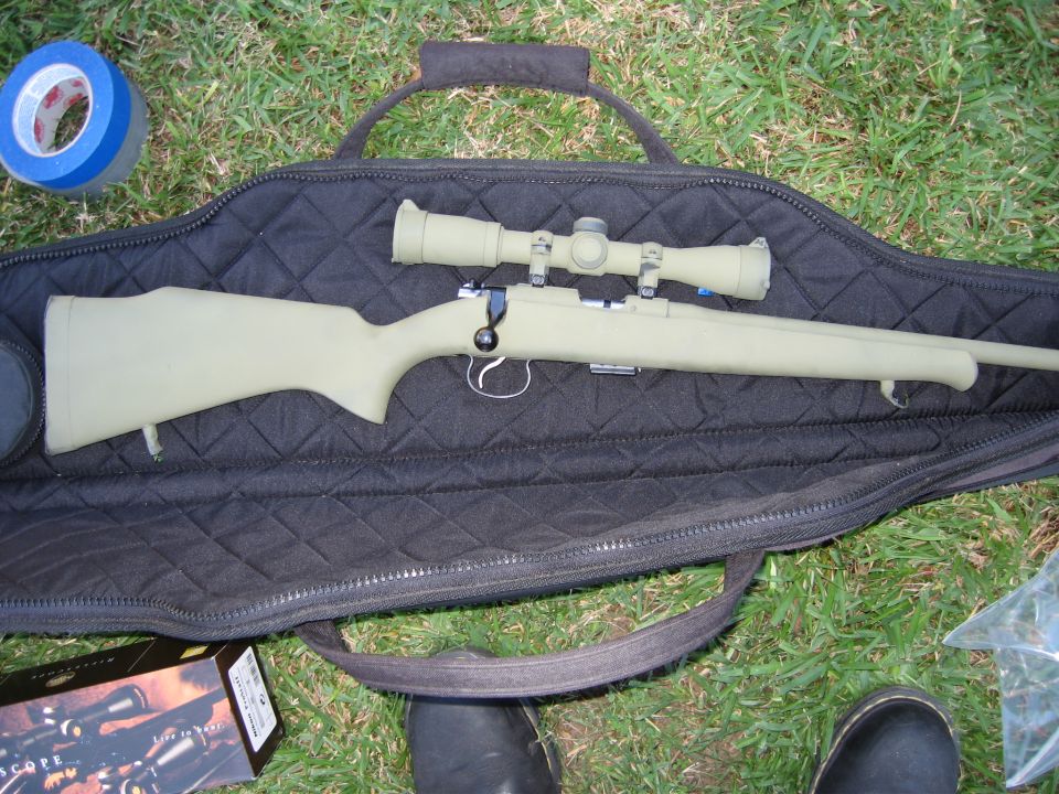 Green bolt-action rifle with scope lying on open black soft gun case on grass