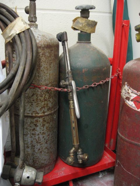 1974 Ford F-100 - A welding torch is attached to a green gas cylinder, with other cylinders nearby on a red cart.