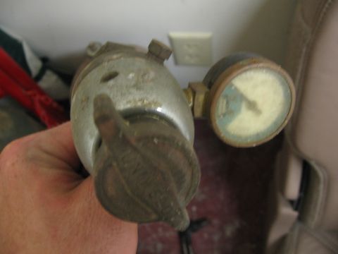 1974 Ford F-100 - A pressure regulator with a gauge is held in a hand, with a portion of a vehicle interior visible in the background.