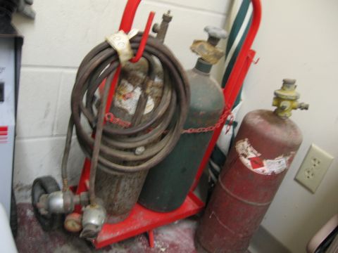 1974 Ford F-100 - A red welding cart holds coiled hoses and two gas cylinders, one green and one red, against a white wall.