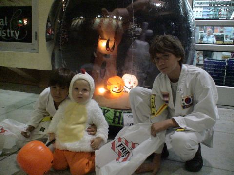 1993 Ford C-350 (Centurion Conversions) - Children dressed for Halloween gather in front of store displays and inflatable decorations.