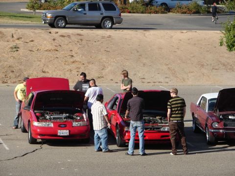 1992 Ford Taurus - A group of people inspect the engine of a red 1992 Ford Taurus at a car meet.