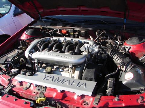 1992 Ford Taurus - The engine compartment of a red car, a Yamaha branded cover and intake system. Another vehicle is visible in the background.