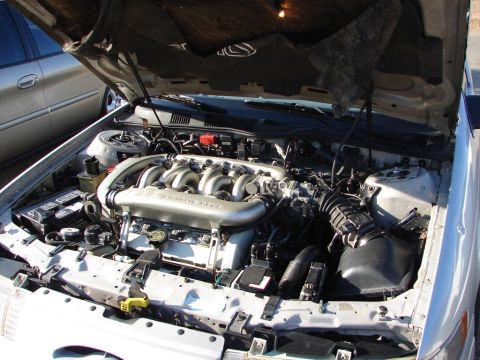 1992 Ford Taurus - The engine bay of a car is shown with the hood open, revealing the engine components. A second vehicle is partially visible on the left sid…
