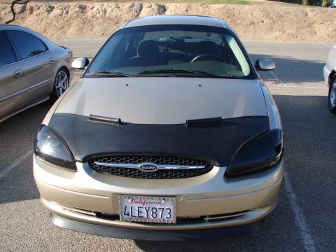 1992 Ford Taurus - This gold sedan features a black car bra and tinted headlights, seen from the front.