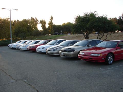1992 Ford Taurus - A row of sedans is parked in a lot, with a red 1992 Ford Taurus coupe in the foreground.