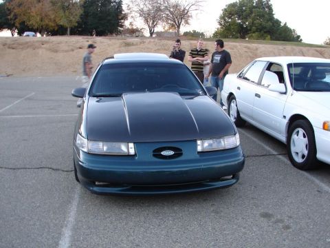 1992 Ford Taurus - Two sedans parked outdoors, one is a dark green 1992 Ford Taurus with a custom hood.