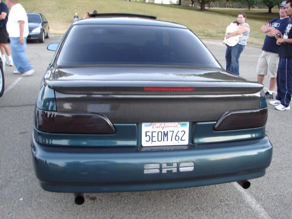 Rear view of a teal sedan with tinted taillights and a carbon fiber trunk accent. License plate reads 5EOM762