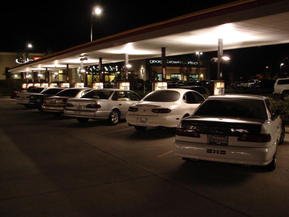 White sedan with black trunk and spoiler, parked at night. License plate visible