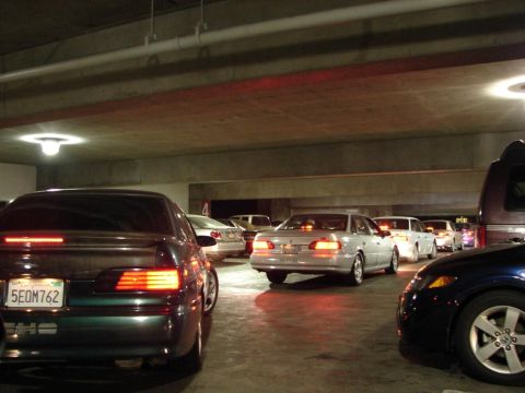 1992 Ford Taurus - Multiple vehicles are parked in a line within a dimly lit parking garage structure.