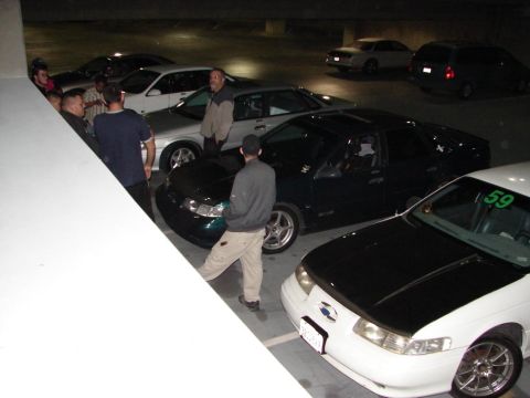 1992 Ford Taurus - A group of people stand around several cars, including a white 1992 Ford Taurus with a black hood.