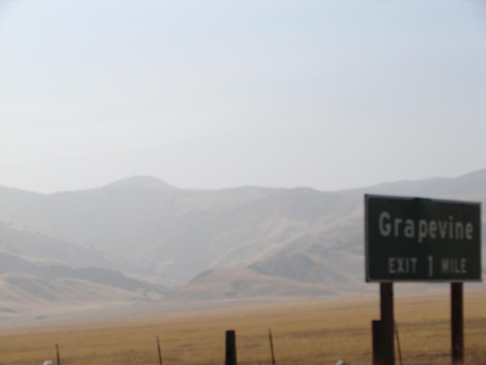 Grapevine exit 1 mile sign with hazy mountains behind