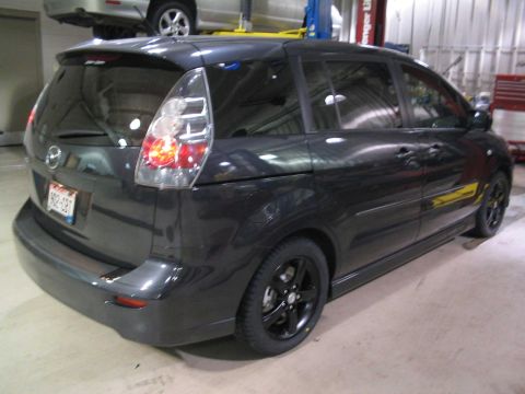 2006 Mazda Mazda 5 - The rear of a dark minivan is shown in a garage setting, black aftermarket wheels.