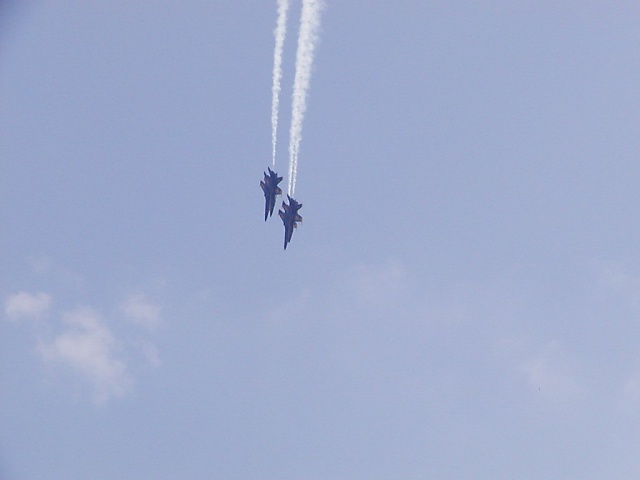 Two fighter jets in formation, leaving contrails against a blue sky