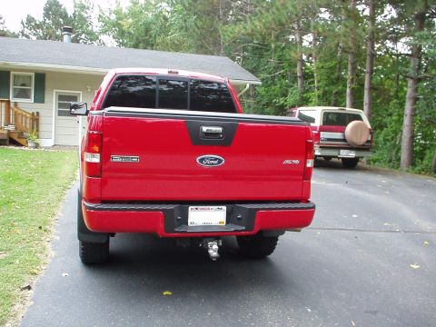 1994 Ford Bronco - A red Ford F-150 pickup truck is parked in front of a house, with a white Ford Bronco visible in the background.