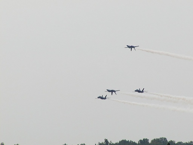 Four fighter jets flying in formation, leaving smoke trails against a hazy sky