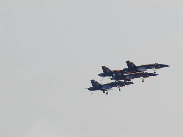 Four dark fighter jets in formation against a pale sky