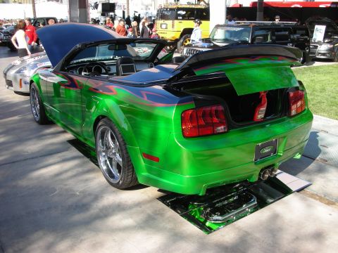 1998 Ford Crown Victoria - bright green Ford Mustang convertible with flame graphics sits with its trunk open at a crowded outdoor car show.