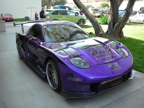 1998 Ford Crown Victoria - purple wide-body sports car with a front splitter and many sponsor decals including BASF sits under a tree at an outdoor show.