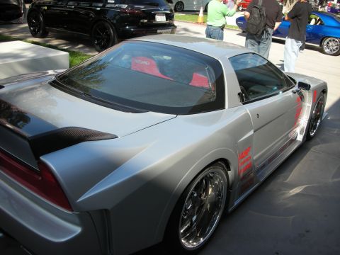 1998 Ford Crown Victoria - silver wide-body two-seat sports car with a red interior and custom chrome wheels is displayed outdoors as spectators walk by.