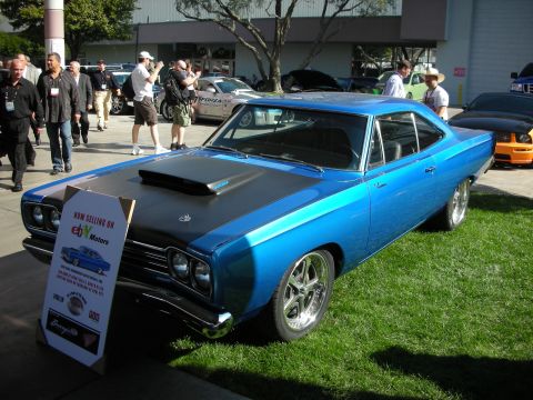 1998 Ford Crown Victoria - blue two-door muscle car with a black hood and scoop sits on grass beside an eBay Motors for-sale sign as people photograph it.