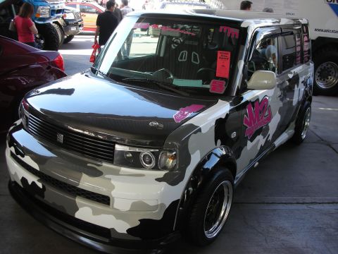 1998 Ford Crown Victoria - boxy compact wagon wrapped in black-and-white urban camouflage sits lowered on chrome wheels at an indoor automotive display.