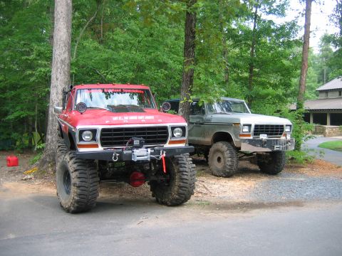 1992 Ford Mustang - Two modified Ford pickup trucks are parked side-by-side in a wooded area with a building in the background.