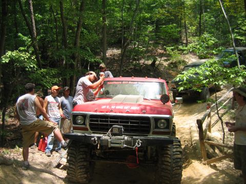 1992 Ford Mustang - A group of people gather around a modified red truck on a wooded trail.