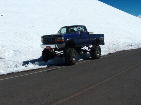 1974 Ford F-100 - A blue pickup truck with oversized tires is parked on the side of a road with snow on the ground.