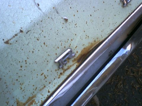 1973 Ford Ranchero - Close-up of a weathered car's emblem and trim, showing signs of age and rust.