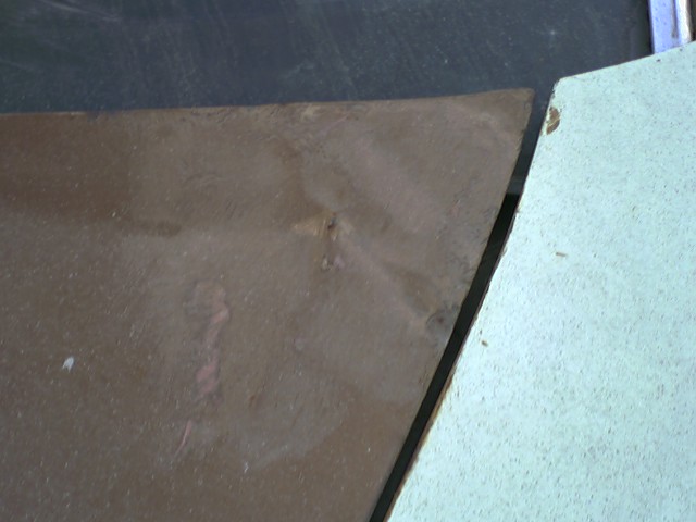 Close-up of a brown metal panel showing rust spots and a seam with a light blue panel