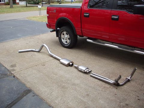 1994 Ford Bronco - Exhaust system components are placed on the ground beside a red pickup truck.