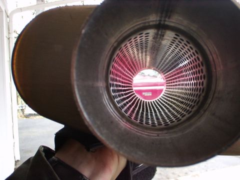 1994 Ford Bronco - The interior of an exhaust pipe is shown, revealing a red circular logo with text through its perforated metal screen.