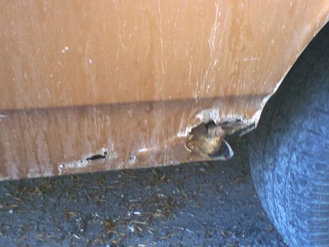 1973 Ford Ranchero - Rust perforations are evident on the lower body panel of an orange vehicle, with a tire visible on the right side.