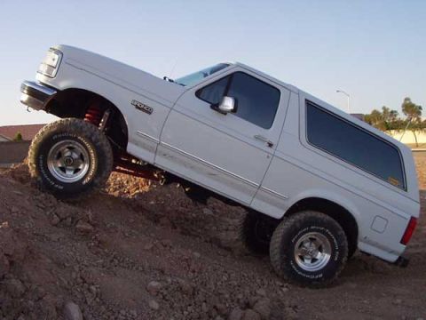 1993 Ford Bronco - A white 1993 Ford Bronco is shown on a dirt incline, highlighting its lifted suspension and off-road capabilities.