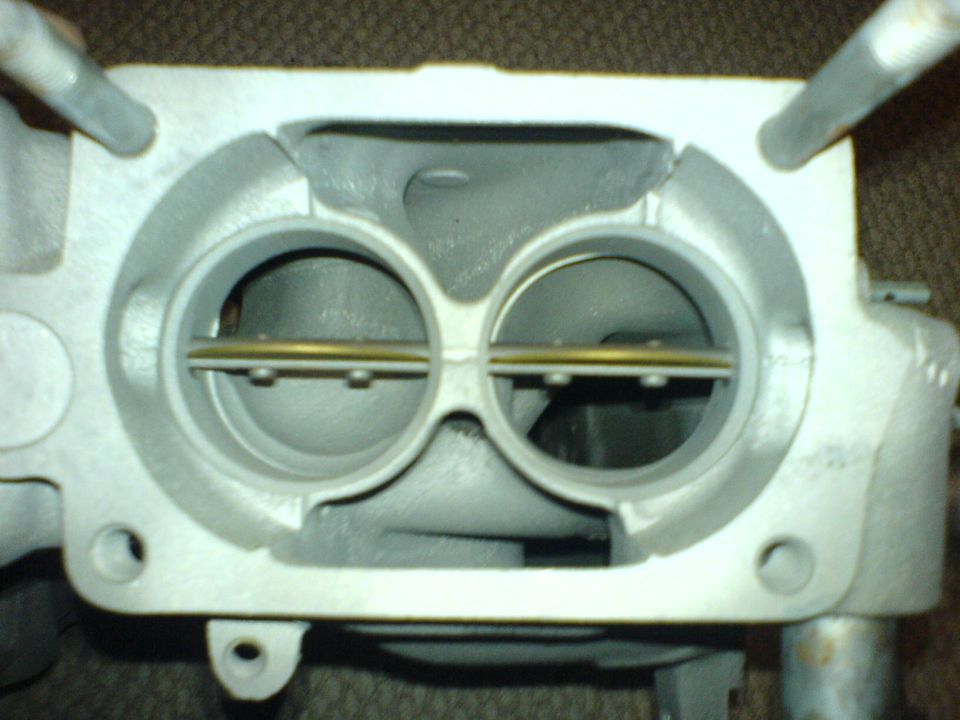 Throttle body with two circular openings and a brass bar across them. Metal casting is gray