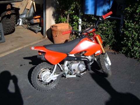 1985 Ford Bronco II - A small orange dirt bike sits on asphalt in front of an open garage door.