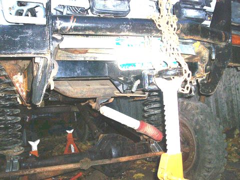 1978 Ford Bronco - Undercarriage of a vehicle supported by jack stands, with a chain hoist attached to the frame.