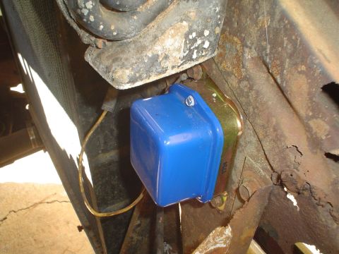 1967 Ford F-250 - Close-up of a blue electrical component with a yellow wire, attached to a heavily rusted metal frame.