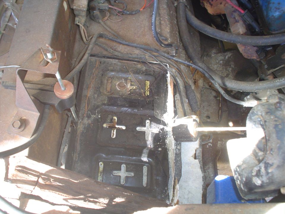 Close-up of a rusty battery tray with wires and engine components in a vehicle's engine bay