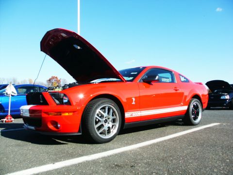 2001 Mercury Grand Marquis - A bright red Ford Mustang Shelby GT500 is parked with its hood up, alongside other vehicles under a clear blue sky.