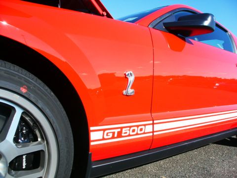 2001 Mercury Grand Marquis - Side view of a red Ford Mustang Shelby GT500, identified by its cobra emblem and GT 500 side stripes.