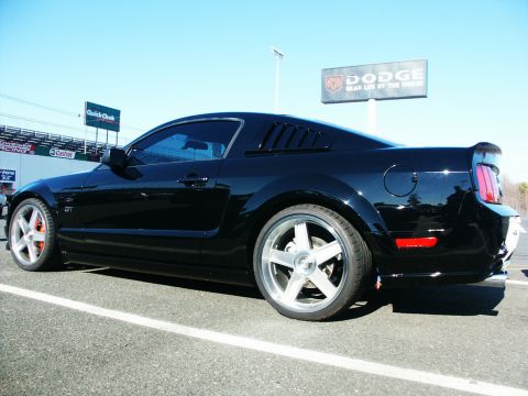 2001 Mercury Grand Marquis - Black Ford Mustang GT parked at a track with Dodge signage in the background.