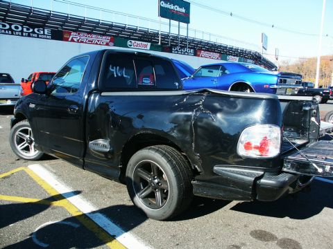 2001 Mercury Grand Marquis - A black pickup truck is parked at a race track with other vehicles visible in the background.