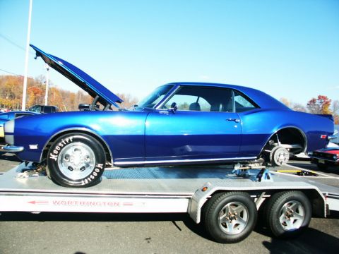 2001 Mercury Grand Marquis - A blue 1967 Chevrolet Camaro coupe is transported on a car carrier with its hood open and missing a rear wheel.