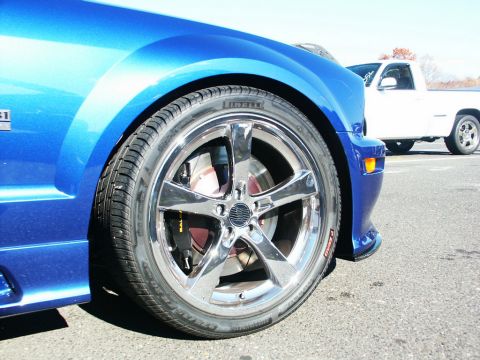 2001 Mercury Grand Marquis - Front wheel and fender of a blue 2005 Ford Mustang GT, with a white pickup truck visible behind it.