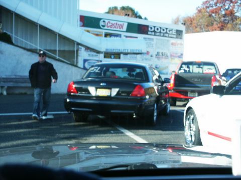 2001 Mercury Grand Marquis - A black 2001 Mercury Grand Marquis sedan is parked on a track with other vehicles and a large billboard in the background.