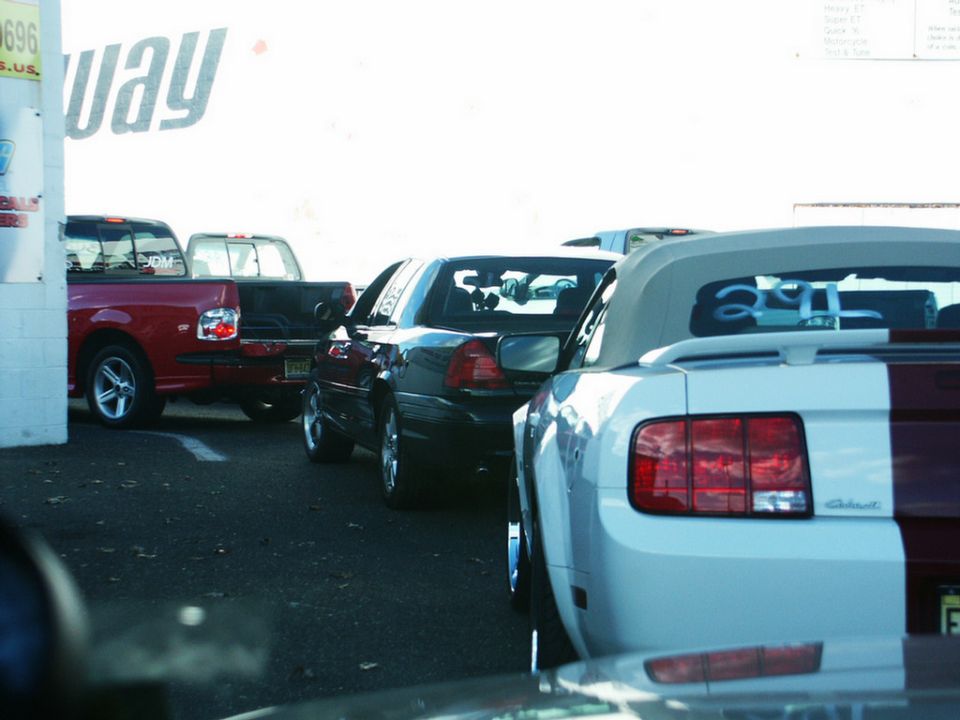 Rear view of a black sedan parked behind trucks