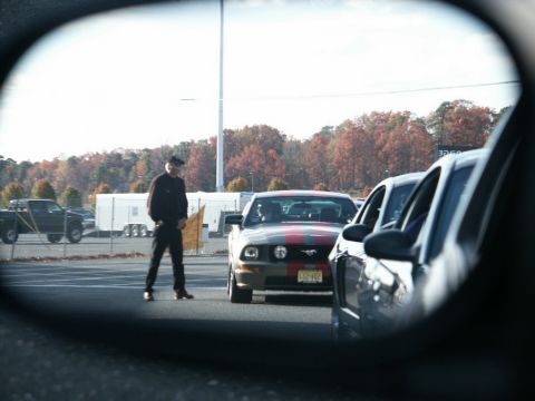 2001 Mercury Grand Marquis - A man stands by a Ford Mustang with racing stripes in a parking lot, viewed from a car's side mirror.